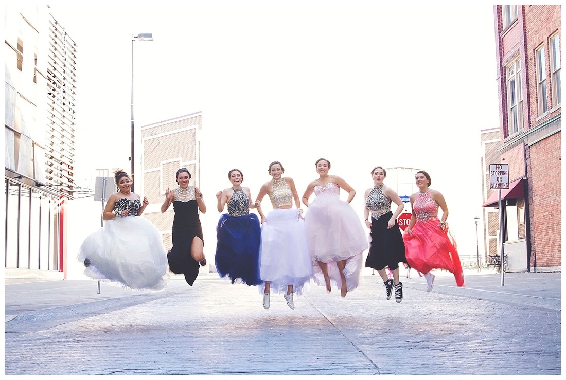 group of girls in prom gowns jumping in the air in downtown green bay wisconsin