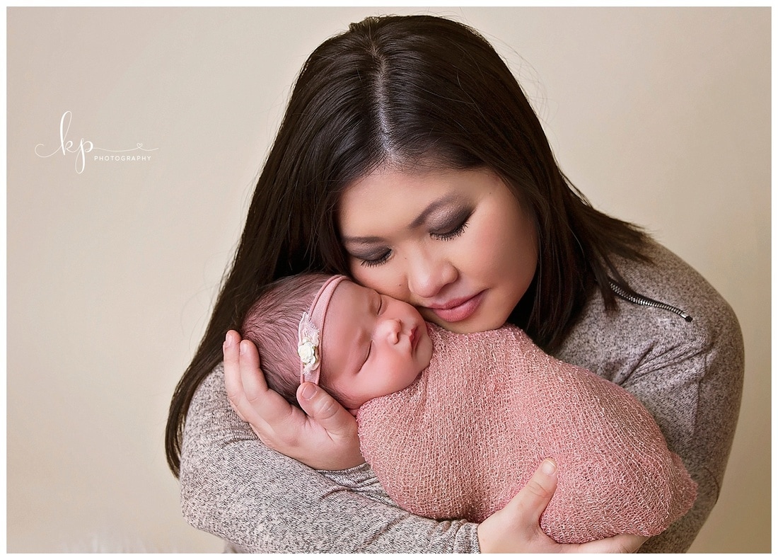newborn baby girl in pink wrap held by mother