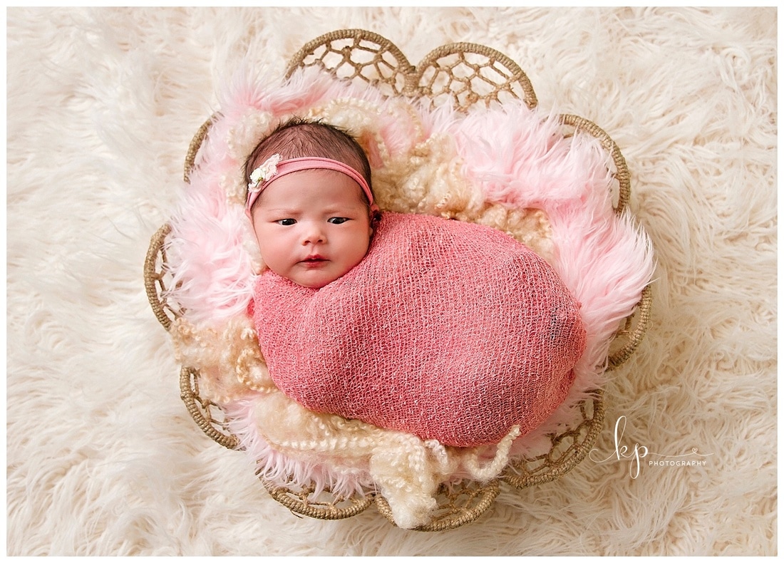 newborn baby girl in pink wrap in round basket