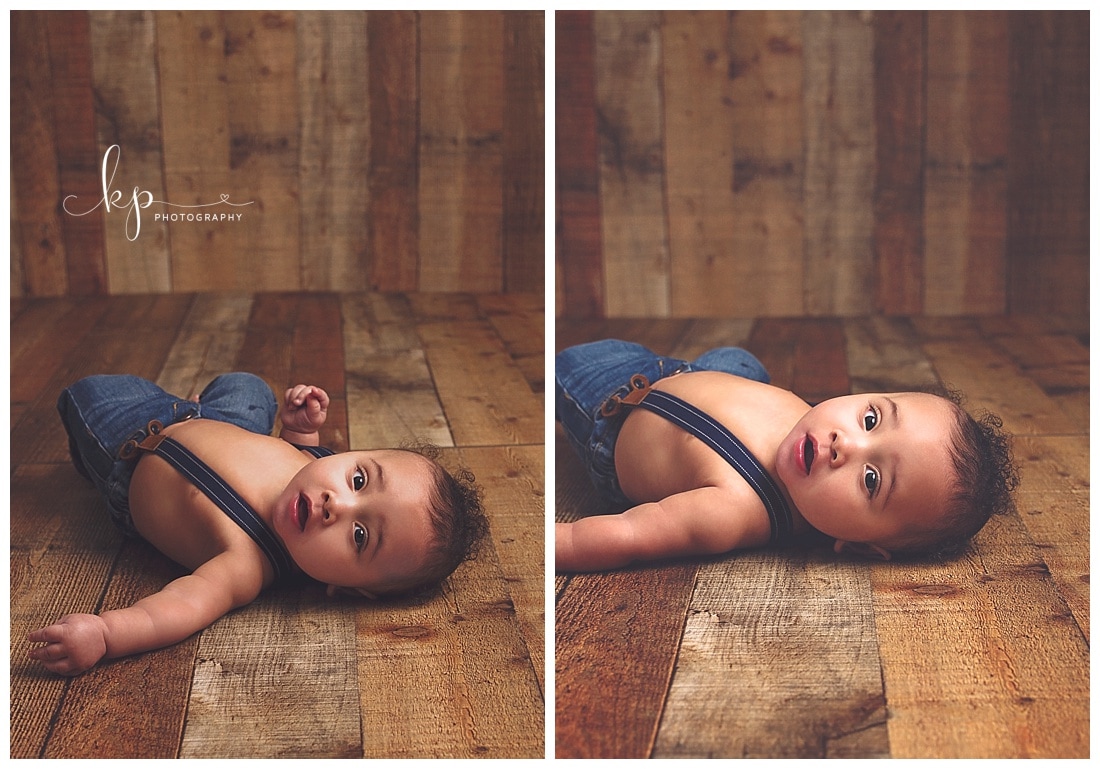 6 month old wearing suspenders laying on wood floor