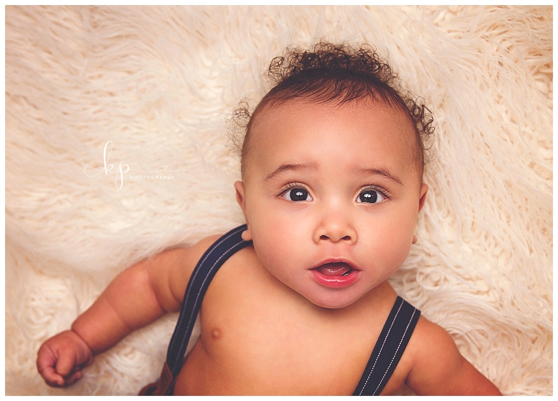 6 month old boy wearing suspenders on white fur rug